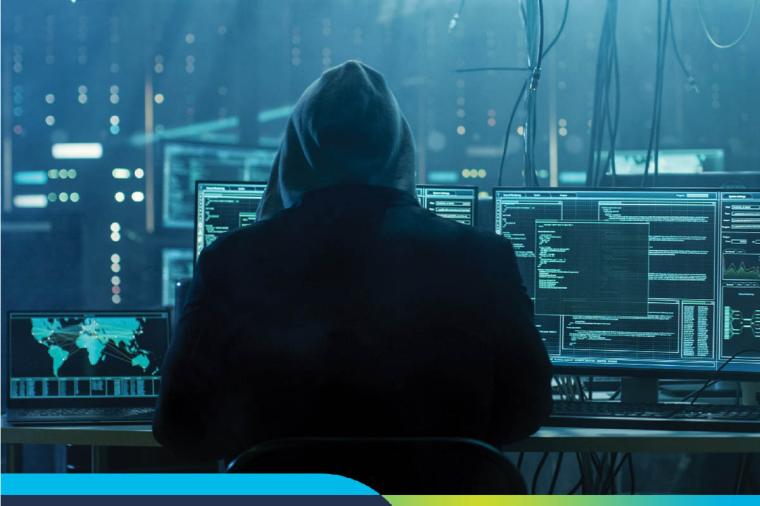 Hooded figure with his back to the camera looking at multiple computer screens