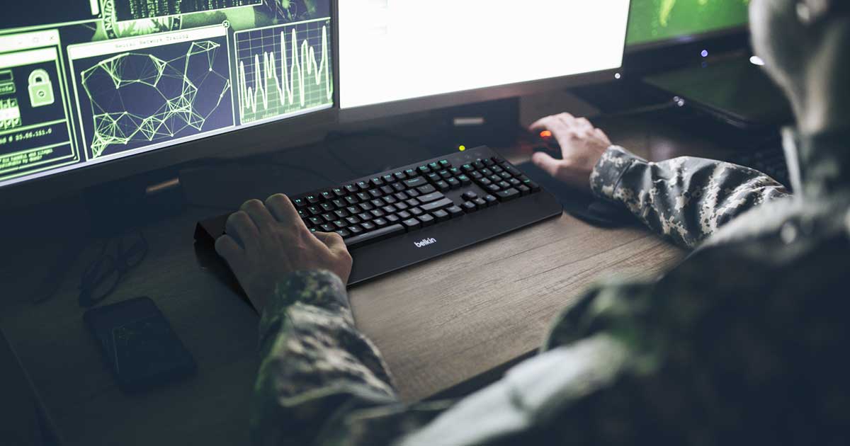 Man in uniform typing on a Belkin keyboard at a command center