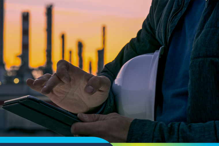 Man holding hard hat in front of oil refinery