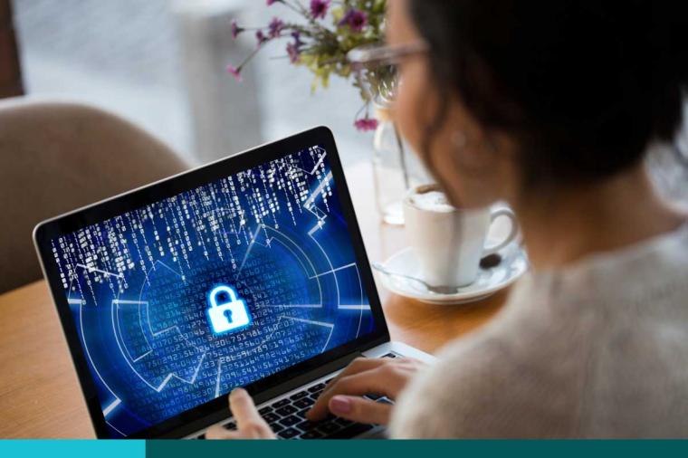 Woman looking down at a laptop. Screen has a locked padlock on it. Coffee cup and small vase of flowers on the table.