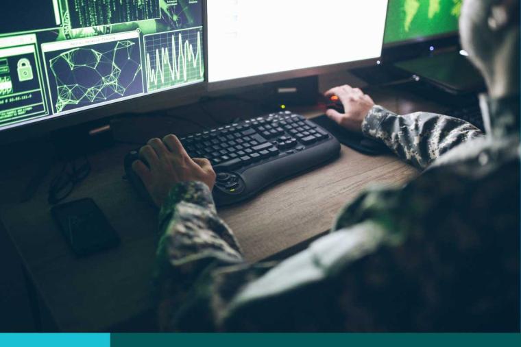 Navy personnel working typing on a keyboard in front of a large computer screen showing data ad graphs