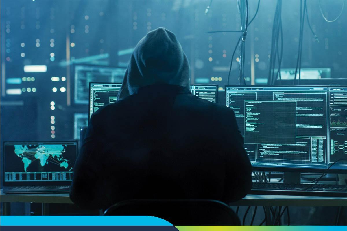 Hooded figure with his back to the camera looking at multiple computer screens