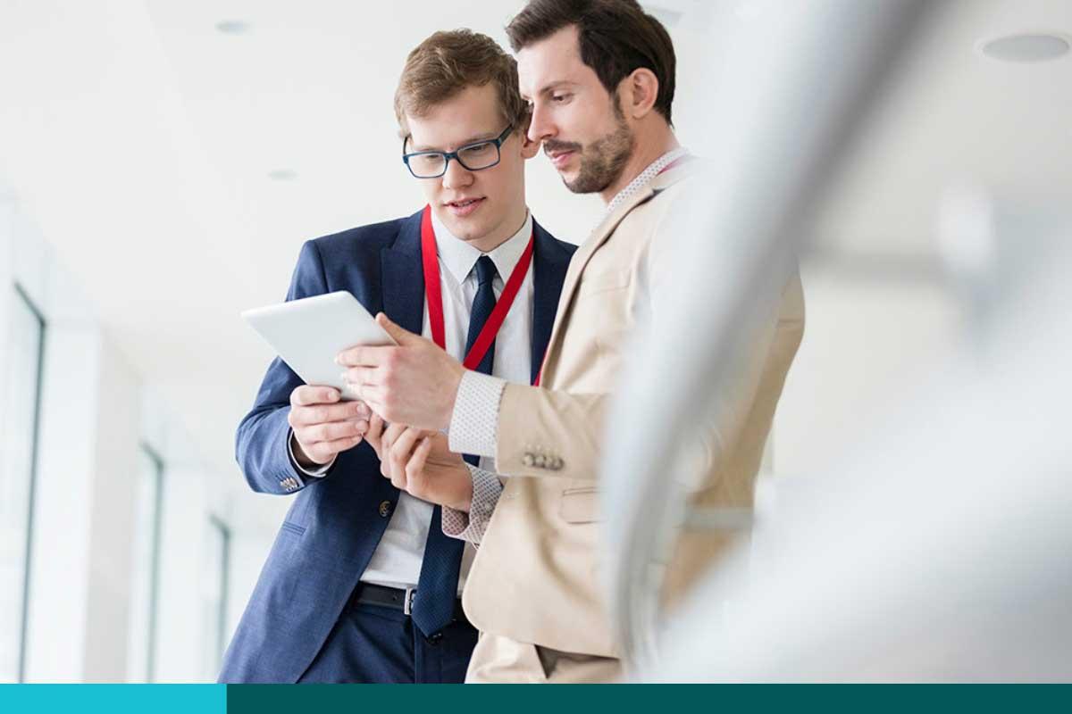 Two men in business suits reading off of a tablet